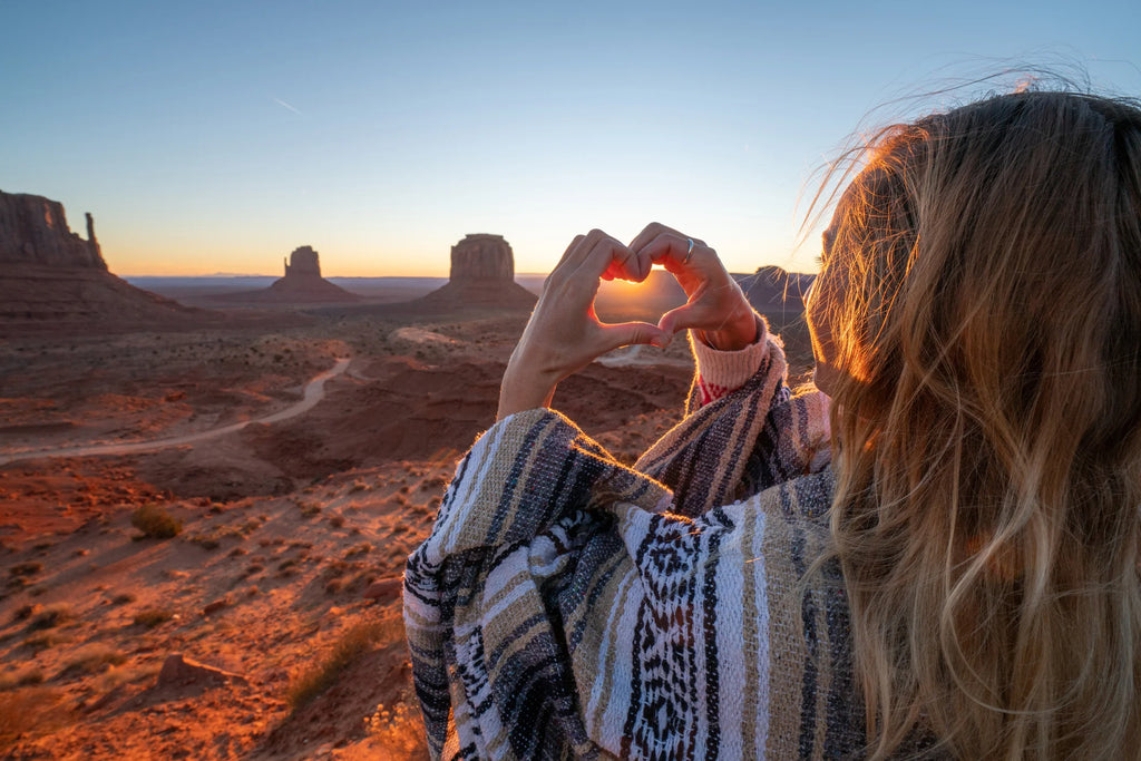Woman making a heart sign with her fingers while looking over Monument Valley.